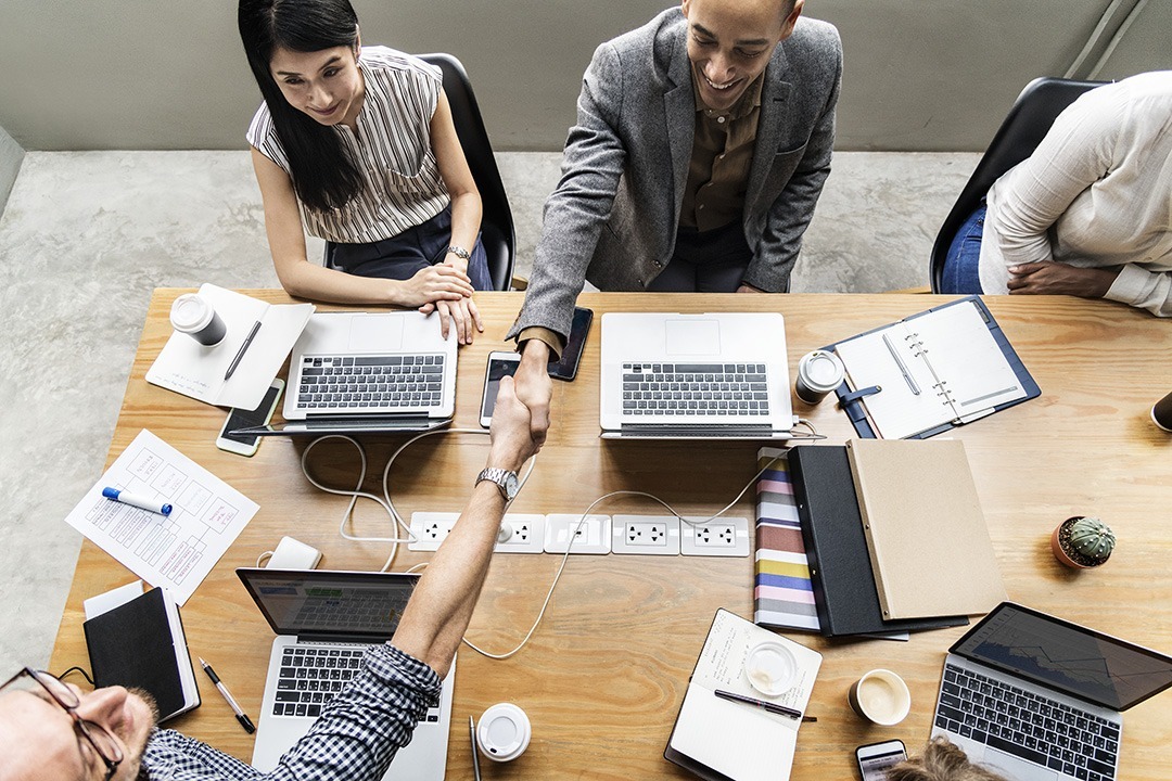 Healthcare Stakeholders shaking hands across a meeting table indicating they have come to an agreement and are making a deal.